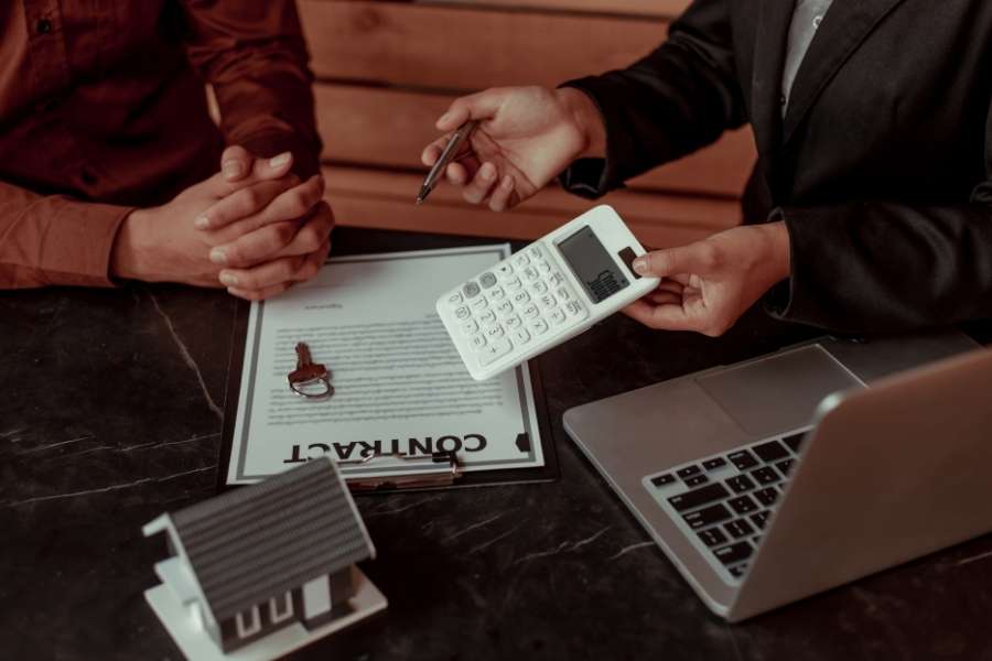 Une personne tient un document comportant l'en-tête "Insurance" tandis qu'une autre s'apprête à signer avec un stylo élégant. Près du papier, une petite clé de voiture et un véhicule miniature rappellent l'objet de la transaction. Cette scène symbolise la finalisation de l'accord et la définition de la prime d'assurance auto.