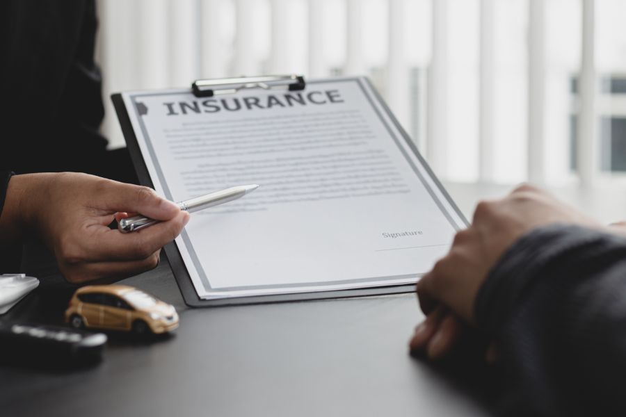 Un conseiller pointe du doigt les clauses d'un contrat d'assurance automobile lors d'un entretien, illustrant un litige ou un refus d'indemnisation.
